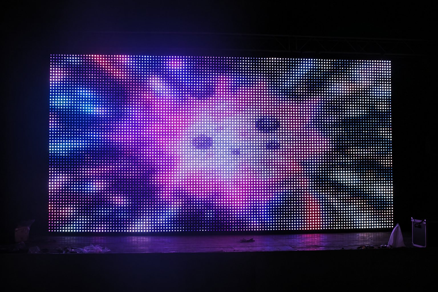 Un grand écran LED composé de petits pixels lumineux affiche des motifs abstraits violets, bleus et blancs dans l'obscurité.
